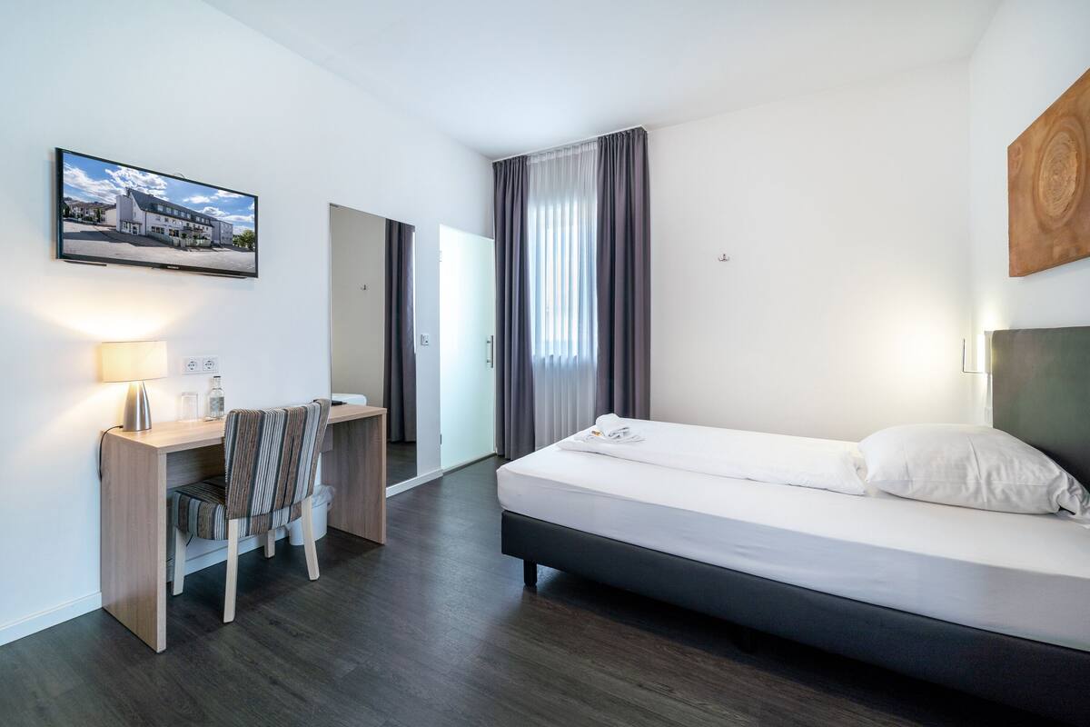 Een hotelkamer met een bed, bureau, stoel en een televisie aan de muur.