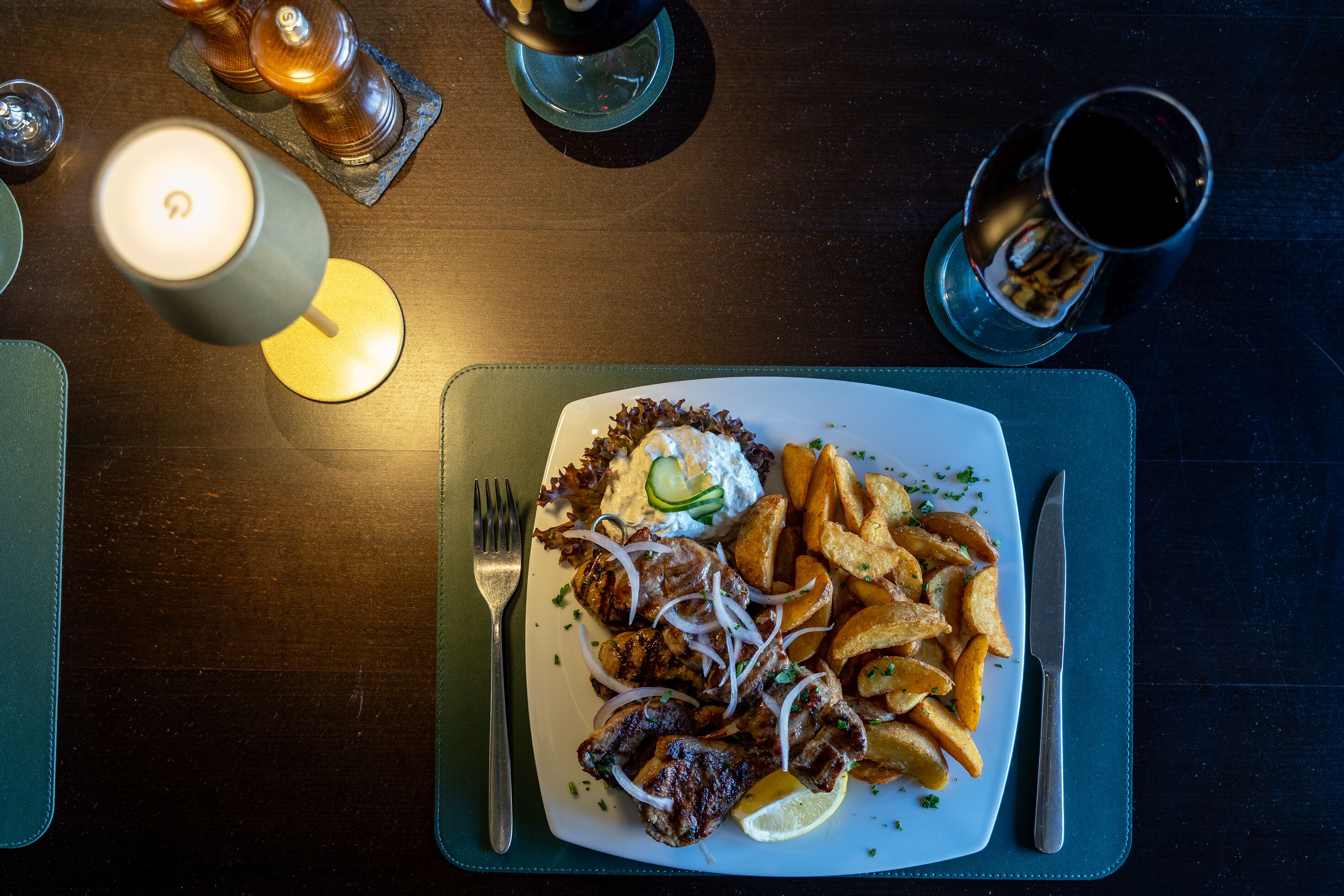 Ein Teller mit gegrilltem Fleisch, Pommes und einem Beilagensalat, dazu liegen Messer und Gabel auf einem dunklen Tisch.