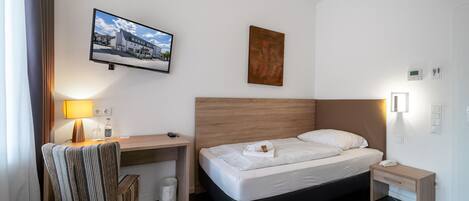 Habitación de hotel con cama, escritorio, silla, lámpara, un cuadro en la pared y una mesita de noche.