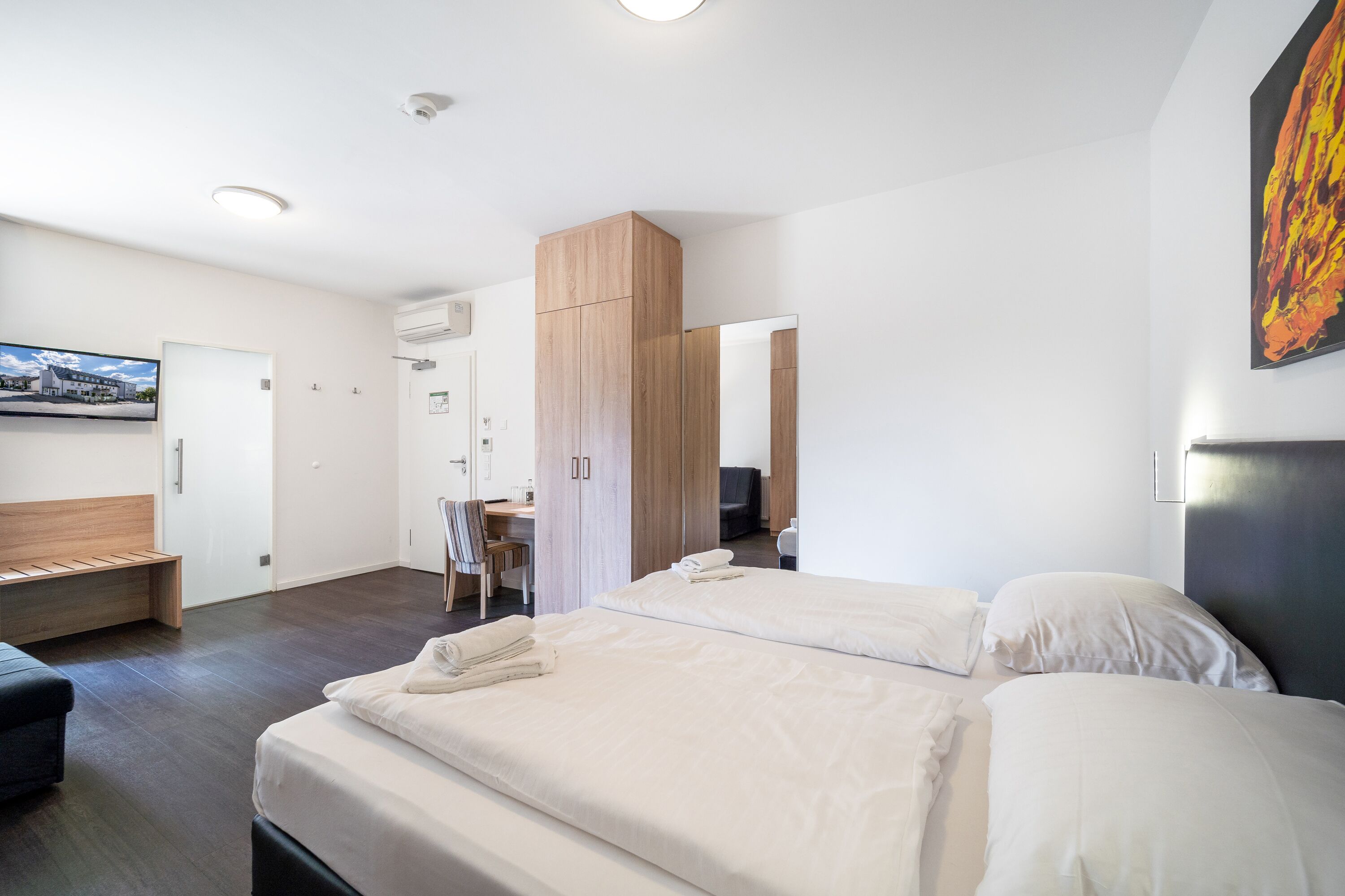 A modern hotel room with two beds, a desk, and a wardrobe.
