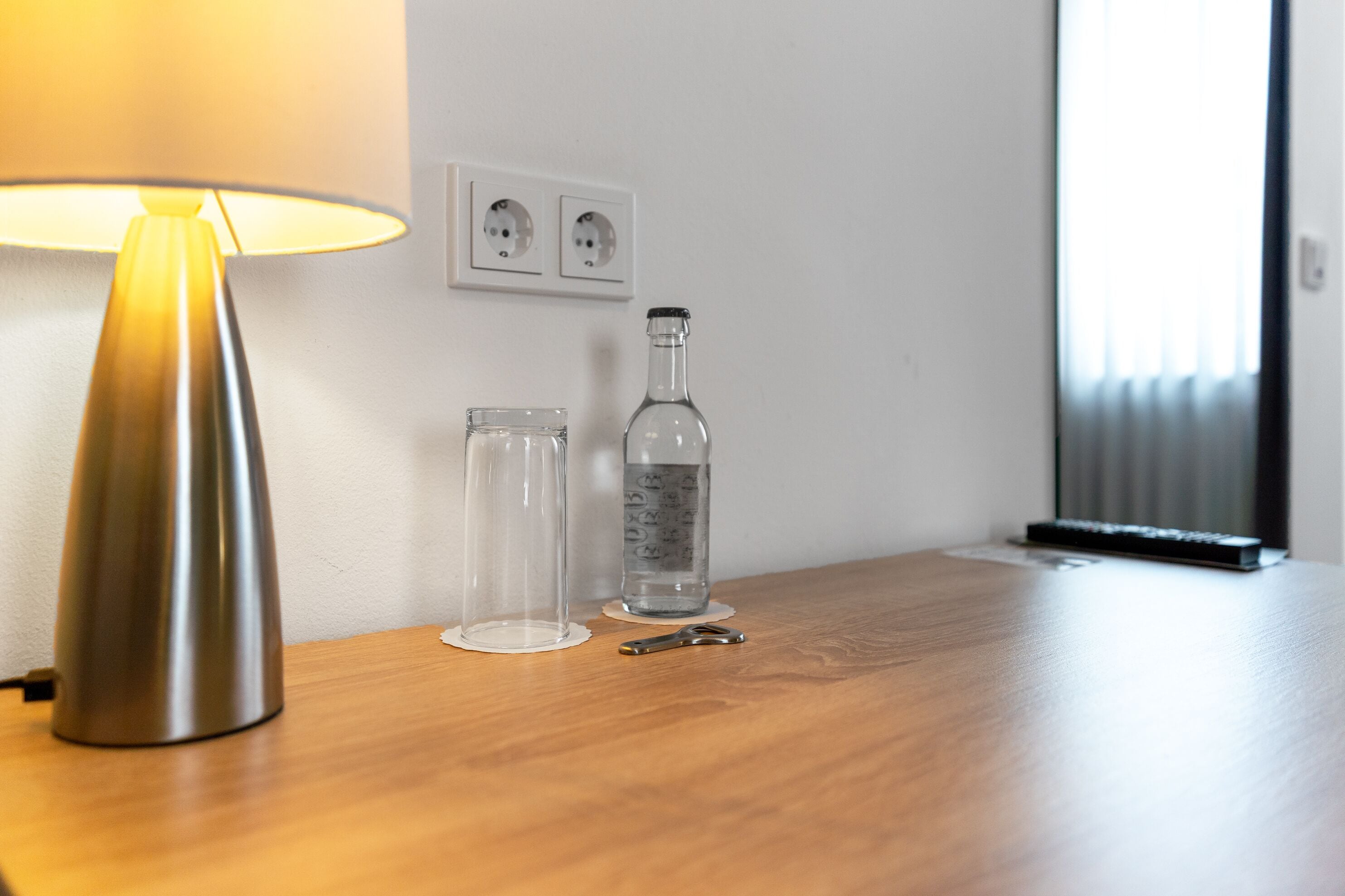 A wooden table with a lamp, a glass bottle, and two clear containers.