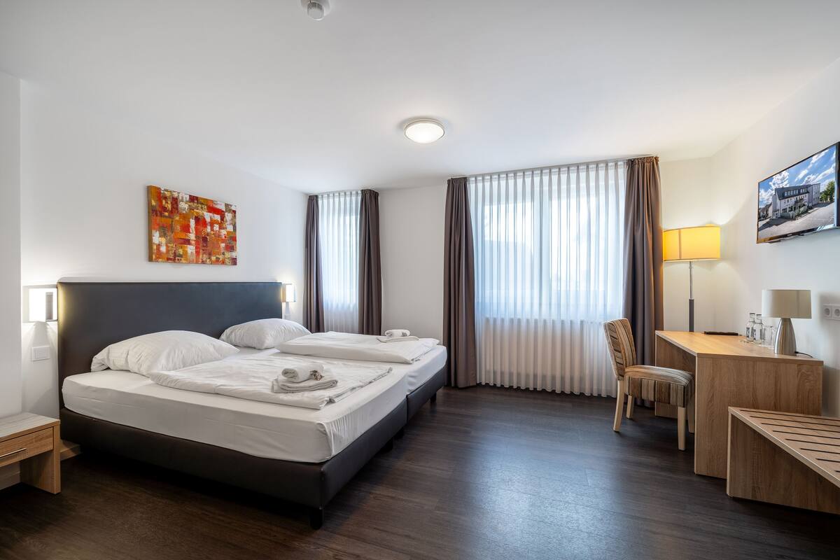 Een hotelkamer met een bed, een bureau, een stoel en een schilderij aan de muur.