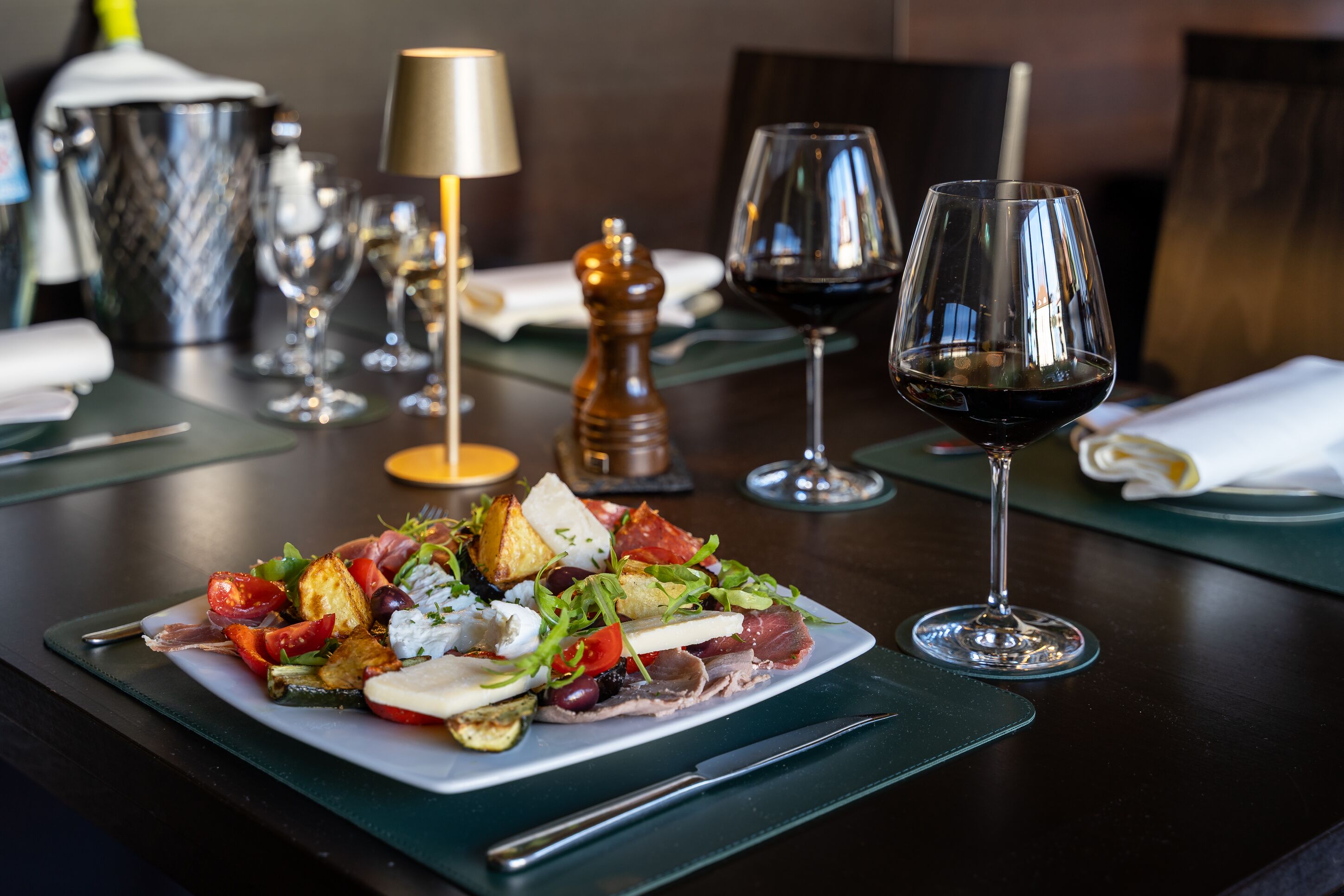 A dining table with a plate of food, a wine glass, and a salt shaker.
