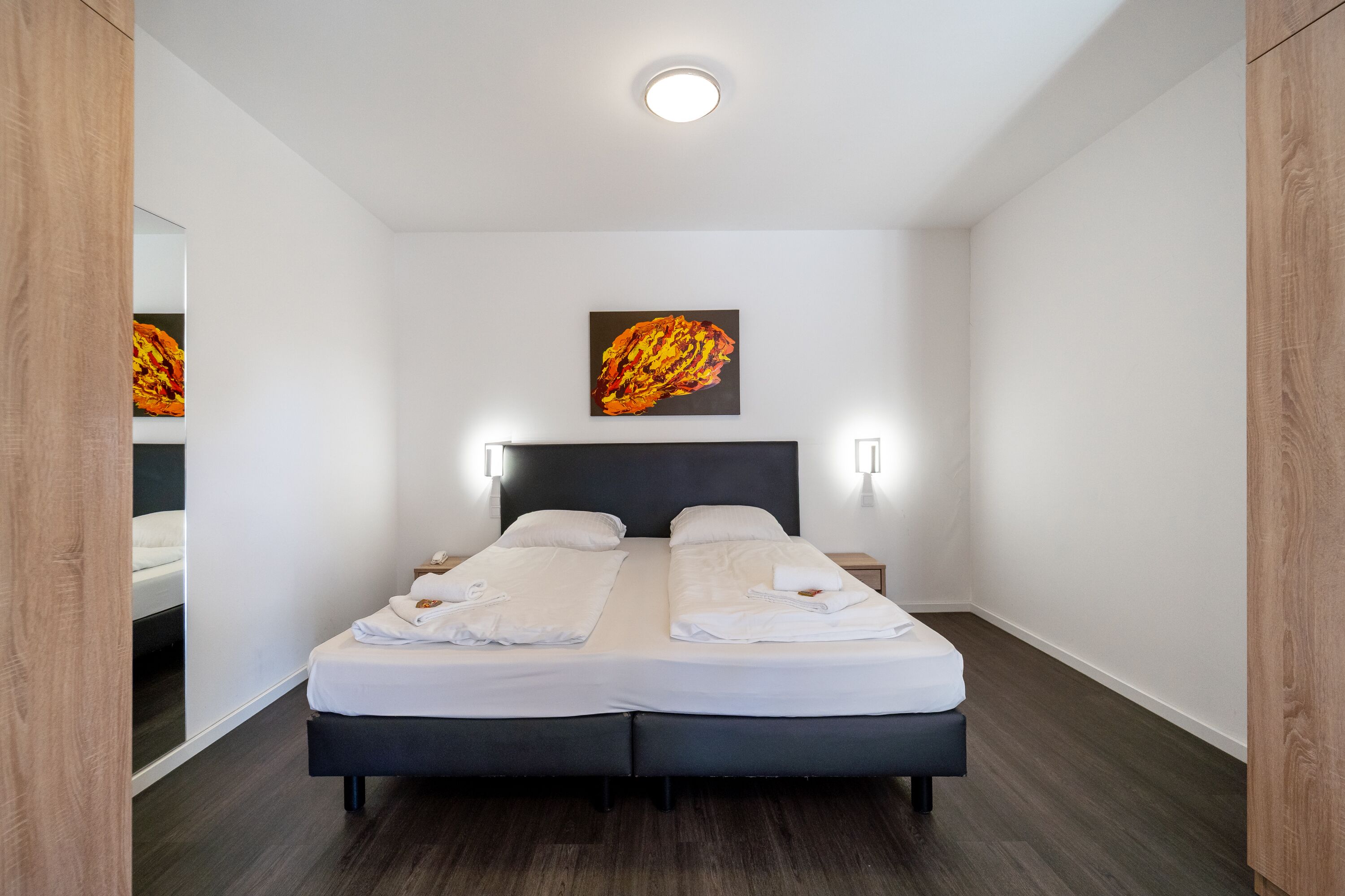 A double bed with white linens, a dark headboard, and a painting on the wall.