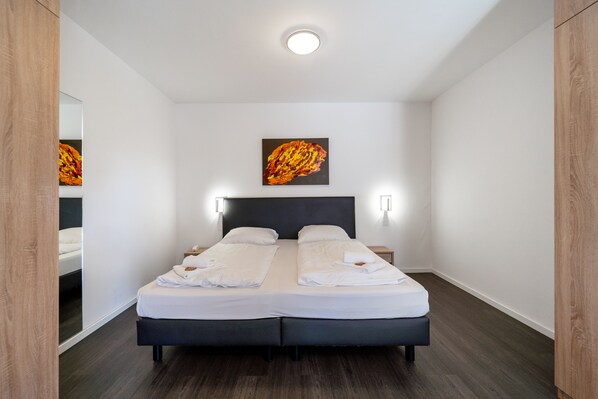 A double bed with white linens, a dark headboard, and a painting on the wall. - Bella Fino Hotel & Suites (Bielefeld)
