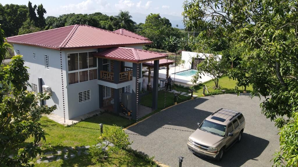 Un edificio de dos plantas con techo rojo, un patio cubierto y una piscina.