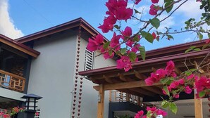 A modern building with a covered patio area, surrounded by lush greenery and vibrant bougainvillea flowers.