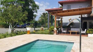 A swimming pool with a pergola, outdoor seating, and a view of a residential building.