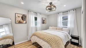 A bedroom with a bed, a mirror, two framed pictures, a bedside table, and a ceiling light fixture. - The Huddle - Near Lambeau Field/Resch Center (Green Bay)