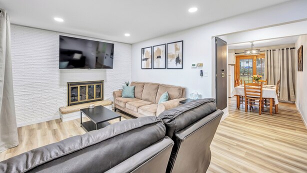A modern living room with a sofa, a TV mounted on the wall, and a dining area with a table and chairs. - The Huddle - Near Lambeau Field/Resch Center (Green Bay)