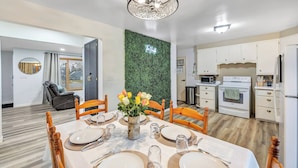 A dining area with a table set for four, a green wall with a neon sign, and a kitchen with white cabinets and appliances. - The Huddle - Near Lambeau Field/Resch Center (Green Bay)