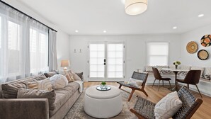 Una sala de estar moderna con sofá, reposapiés, sillas y un comedor con mesa y sillas.