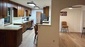 A modern kitchen with wooden cabinets, a central island, and a dining area with a high chair. - Crew-Ready Near Nine Mile Pensacola Stay (Pensacola)