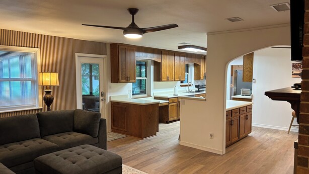 A modern kitchen with wooden cabinets, a central island, and a dining area with a table and chairs. - Crew-Ready Near Nine Mile Pensacola Stay (Pensacola)
