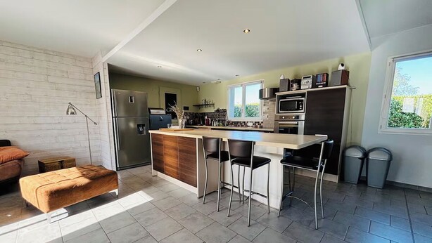 A modern kitchen with a central island, bar stools, and a dining table.