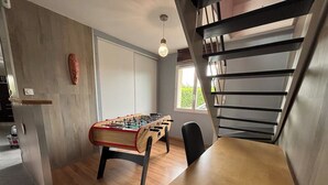 A room with a wooden table, a foosball table, a chair, a staircase, and a window.