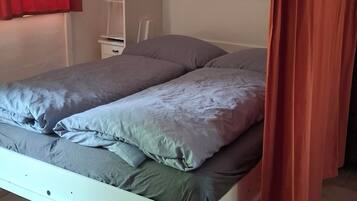 Una cama con estructura blanca, ropa de cama gris y una cortina roja entreabierta.