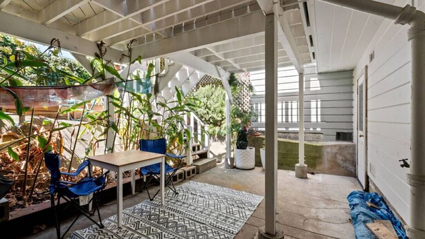Un patio couvert avec une table et des chaises, entouré de plantes en pot et agrémenté d’un tapis à motifs.