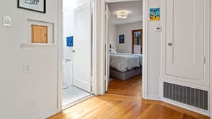 Un couloir menant à une chambre à coucher, qui contient un lit, une porte et une grille d’aération sur le mur.