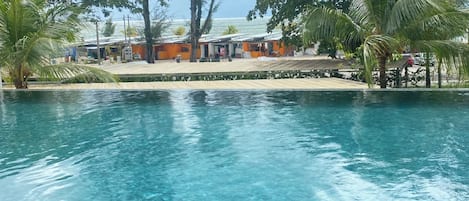 A clear blue pool with a view of a beach and palm trees in the background.