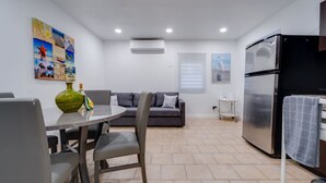 A modern kitchen with a dining area, a grey sofa, and a refrigerator.