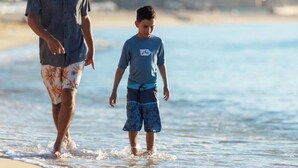 Een man en een kind wandelen over het strand.