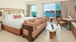 Ruime hotelkamer met een groot bed, een slaapbank, een eettafel en uitzicht op zee.