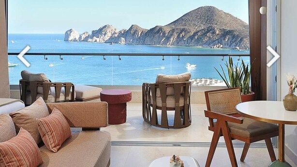 Een balkon met uitzicht op zee en bergen, ingericht met banken, stoelen en een tafel.