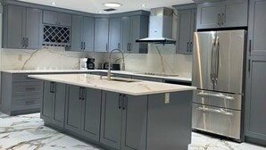A modern kitchen with grey cabinets, a large island, and a stainless steel refrigerator. - Peaceful and newly home with solar heated pool (Brandon)