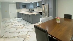 A modern kitchen with grey cabinets, a central island, and a dining area with a wooden table and chairs. - Peaceful and newly home with solar heated pool (Brandon)