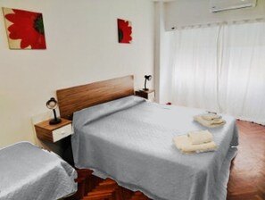 A hotel room with a bed, bedside table, lamp, and a window with curtains.