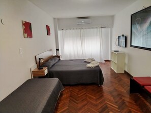 A hotel room with two beds, a desk, a chair, a TV, and a large window with curtains.