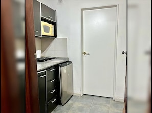 A compact kitchen with a microwave, a small refrigerator, and a cabinet with drawers.