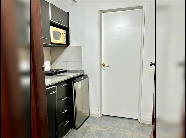 A compact kitchen with a microwave, a small refrigerator, and a cabinet with drawers.