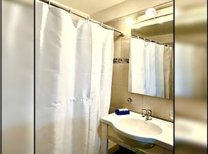 A bathroom with a shower curtain, a sink, and a mirror. - Gran monoambiente en centro de Bs As 1 C (Buenos Aires)