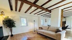 A spacious living room with a wooden ceiling, a sofa, a cowhide rug, a lamp, and a potted plant. - Cozy Family Home near Ramstein Air Base – Comfort & Convenience (Hochspeyer)
