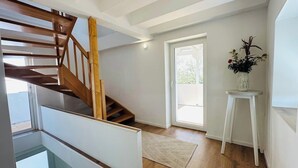 A modern interior with a wooden staircase, a glass door leading outside, and a small white table with a vase of flowers. - Cozy Family Home near Ramstein Air Base – Comfort & Convenience (Hochspeyer)