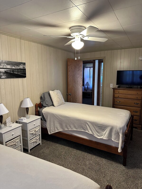 A bedroom with a bed, a nightstand with a lamp, a dresser, a television, and a ceiling fan.