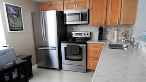 A modern kitchen with stainless steel appliances, wooden cabinets, and a marble countertop. - Seasonal Rental: 1-bedroom condo, gated community, sunrises over Old Tampa Bay (Clearwater)