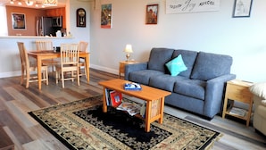 A living room with a sofa, a coffee table, and a dining area with chairs and a table. - Seasonal Rental: 1-bedroom condo, gated community, sunrises over Old Tampa Bay (Clearwater)