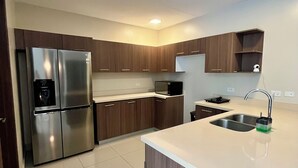 Eine moderne Küche mit einem Edelstahl-Kühlschrank, Holzschränken, einer weißen Arbeitsplatte und einer eingebauten Spüle.