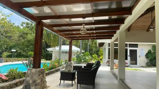 Eine überdachte Terrasse im Freien mit Pool, Steinsäulen und Korbmöbeln.