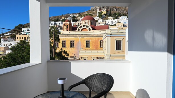 Un balcon avec une table et des chaises, donnant sur une ville aux bâtiments blancs et sur une colline en arrière-plan.
