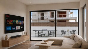 Ein modernes Wohnzimmer mit einem Flachbildfernseher, einem Ecksofa, einem Couchtisch aus Holz und einer Schiebetür zu einem Außenbereich mit einem Tischtennis-Tisch.