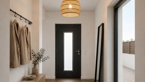 Ein Flur mit einer hölzernen Bank, einem Kleiderständer mit Mänteln, einer Tür mit Milchglasfenster und einem großen Fenster.