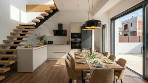 Una cocina moderna con una isla central, un comedor con una mesa larga y una escalera con escalones de madera.
