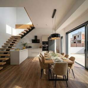 Una cocina moderna con una isla central, un comedor con una mesa larga y una escalera con escalones de madera.