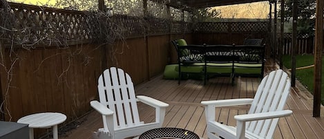 Um deck com lareira, cadeiras Adirondack brancas e área de estar coberta.
