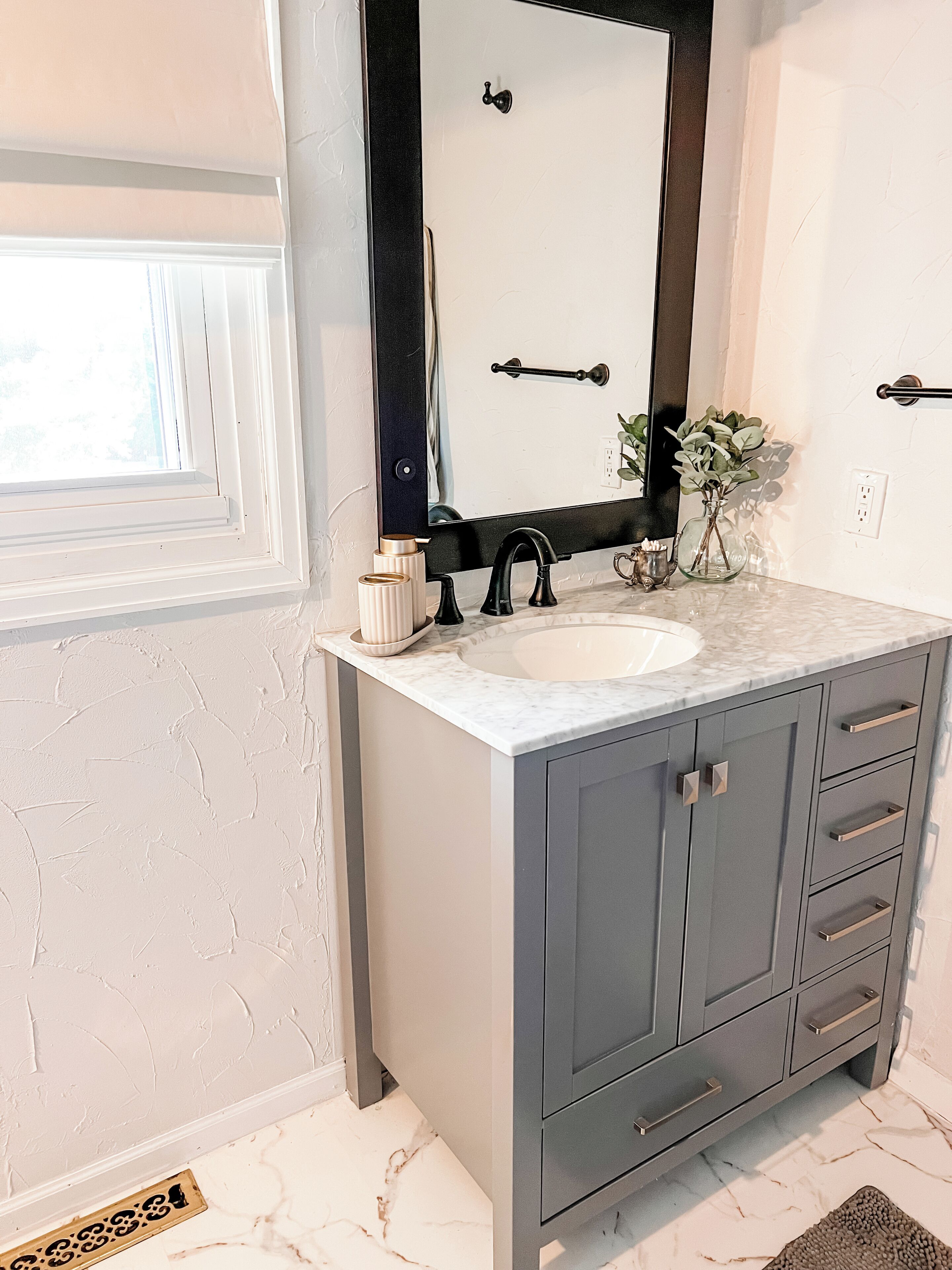 Une salle de bain avec un lavabo en marbre blanc, un robinet noir et un meuble gris doté de tiroirs.