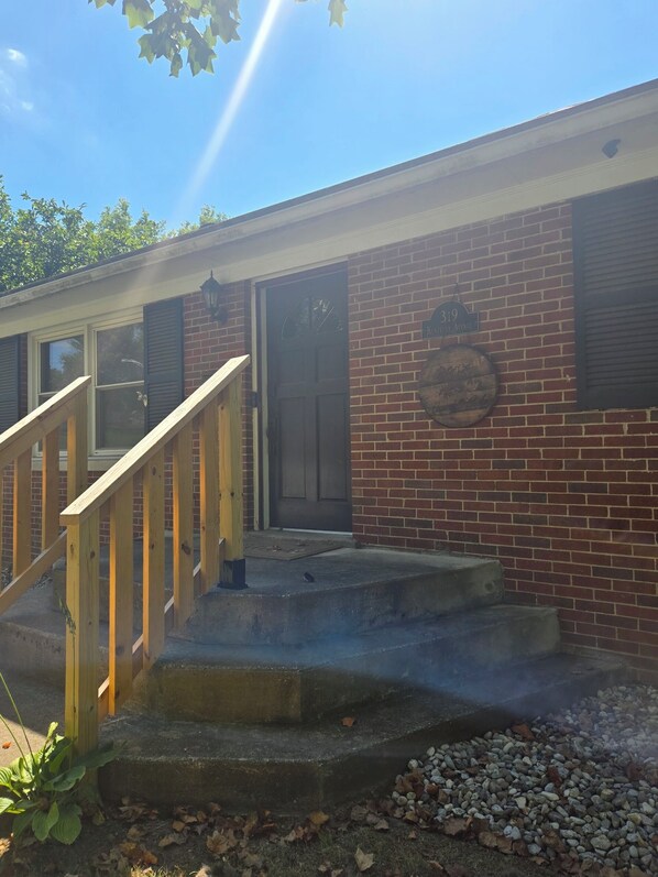 A brick building with a wooden staircase leading to a door, a round metal sign on the wall, and a clear sky above.